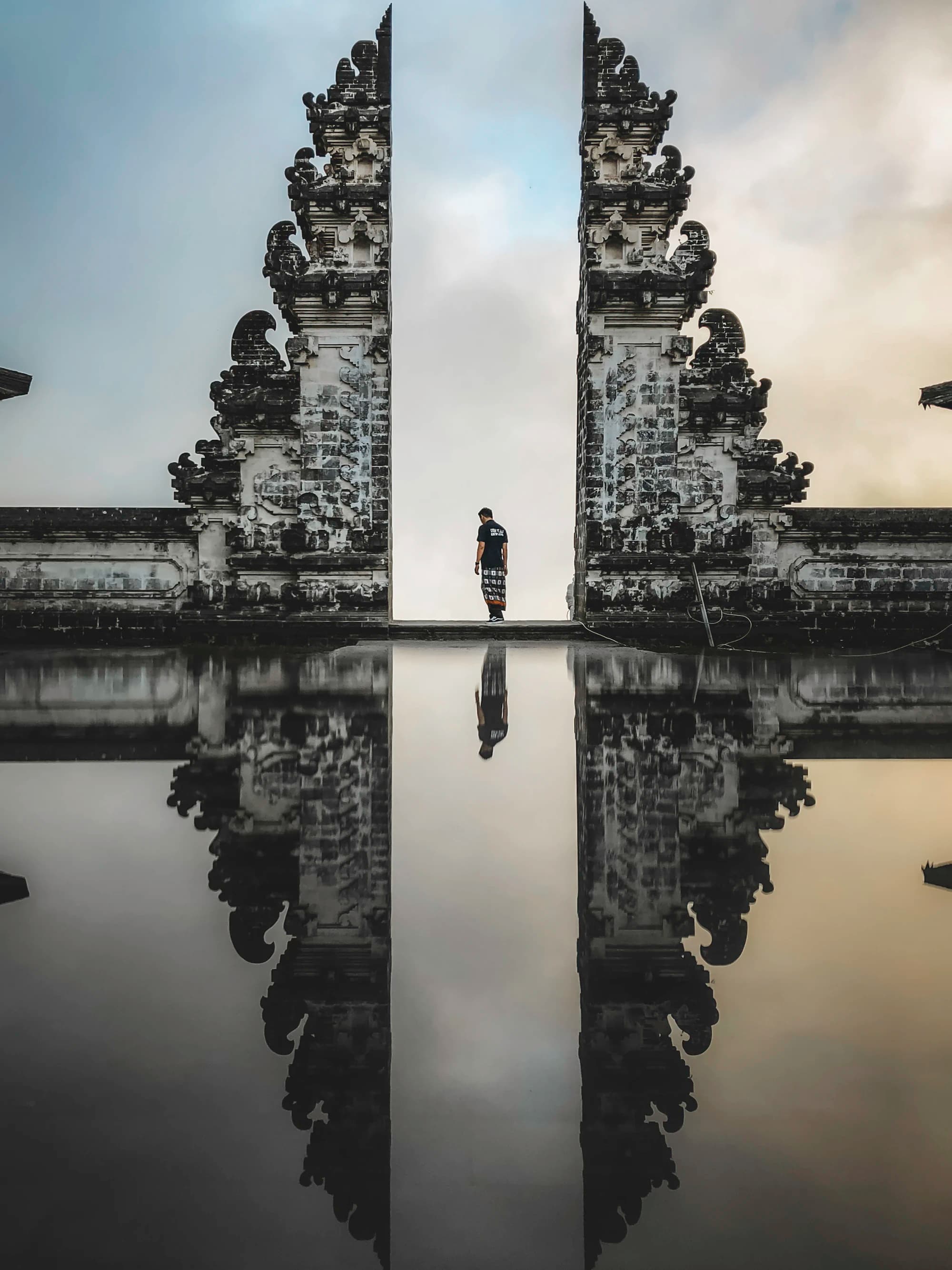 A visitor standing between the split gates of Lempuyang temple, reflected below