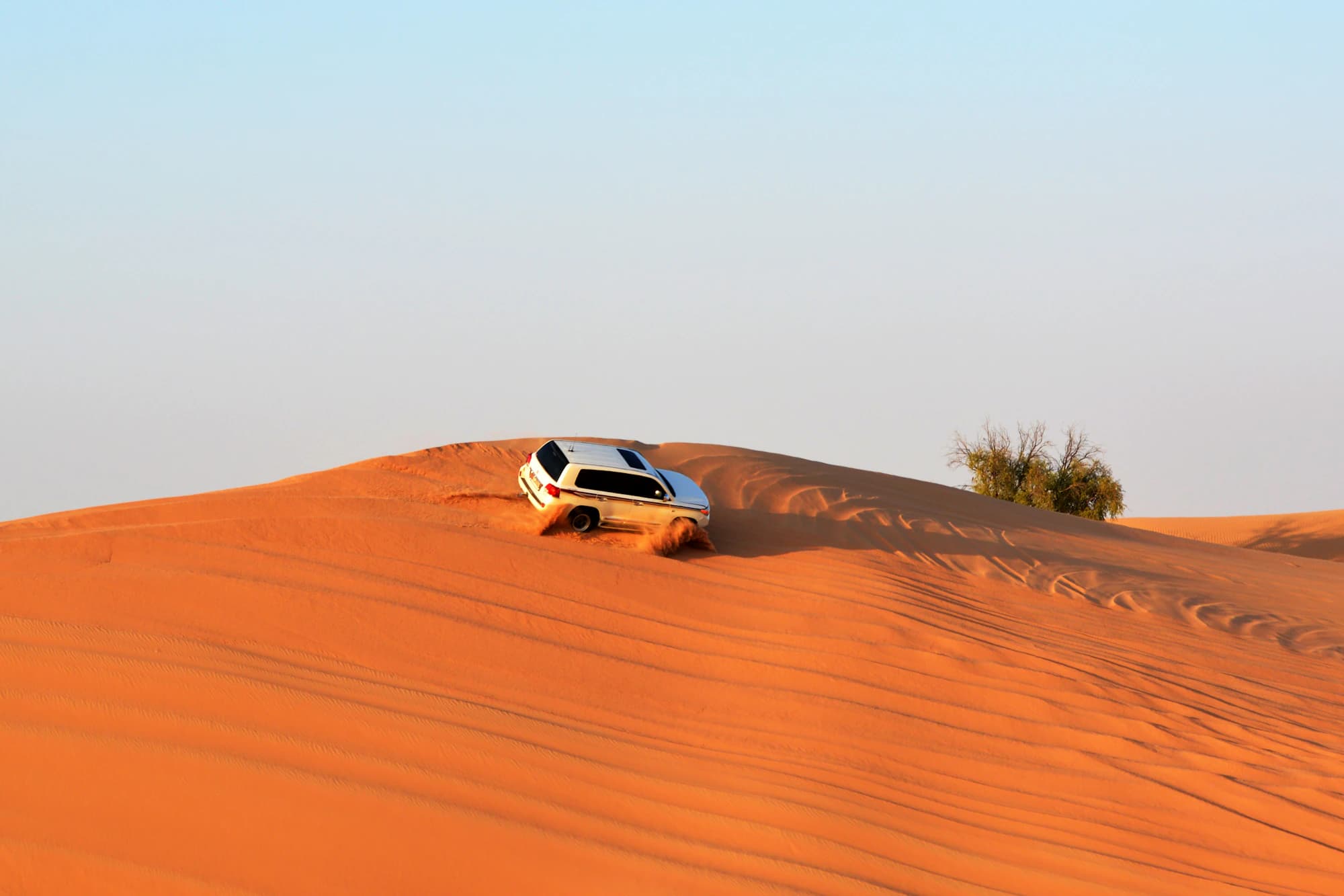 A 4x4 cresting a red sand dune in the desert outside Dubai