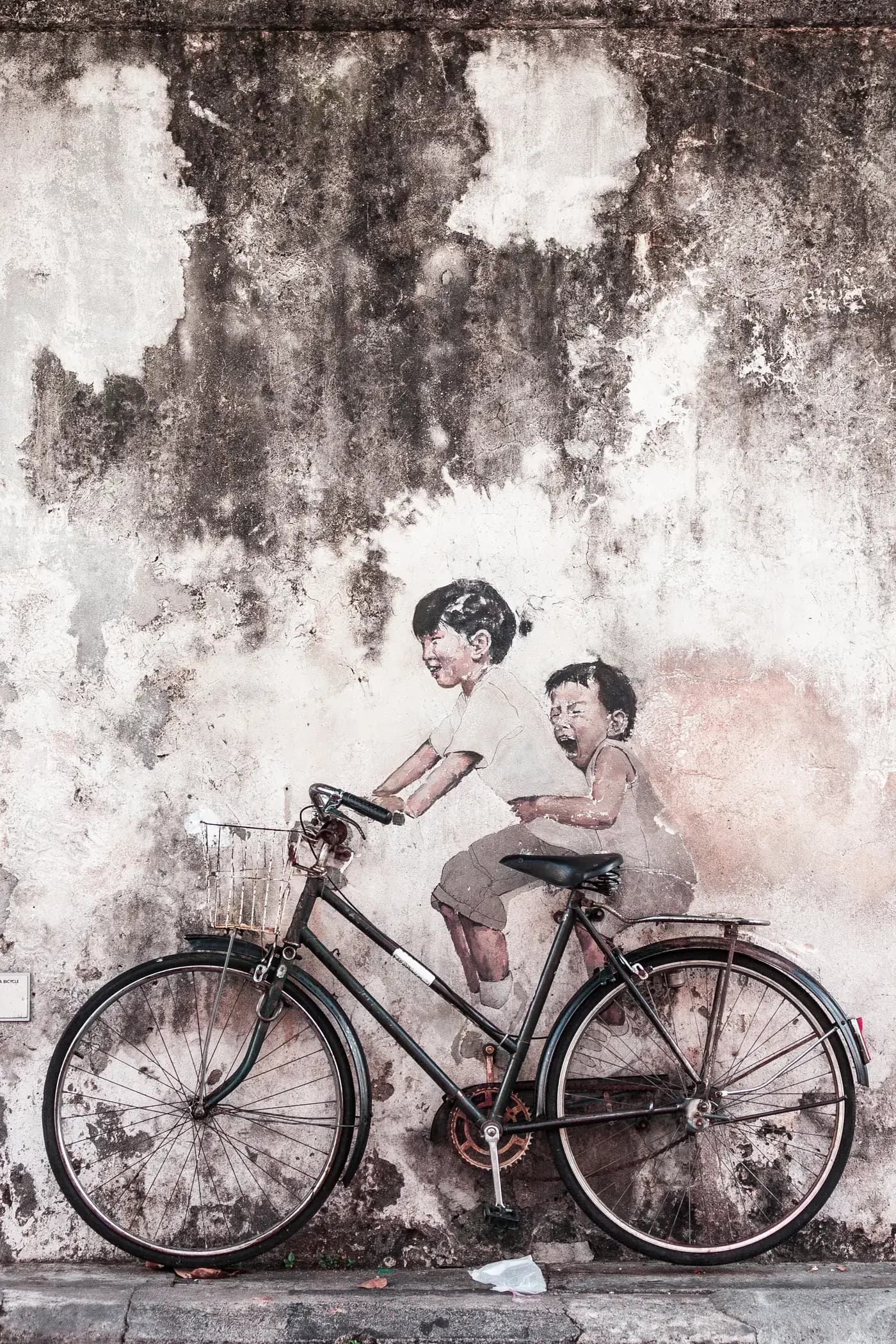 A traveller on a red bicycle beside a street-art mural in George Town, Penang