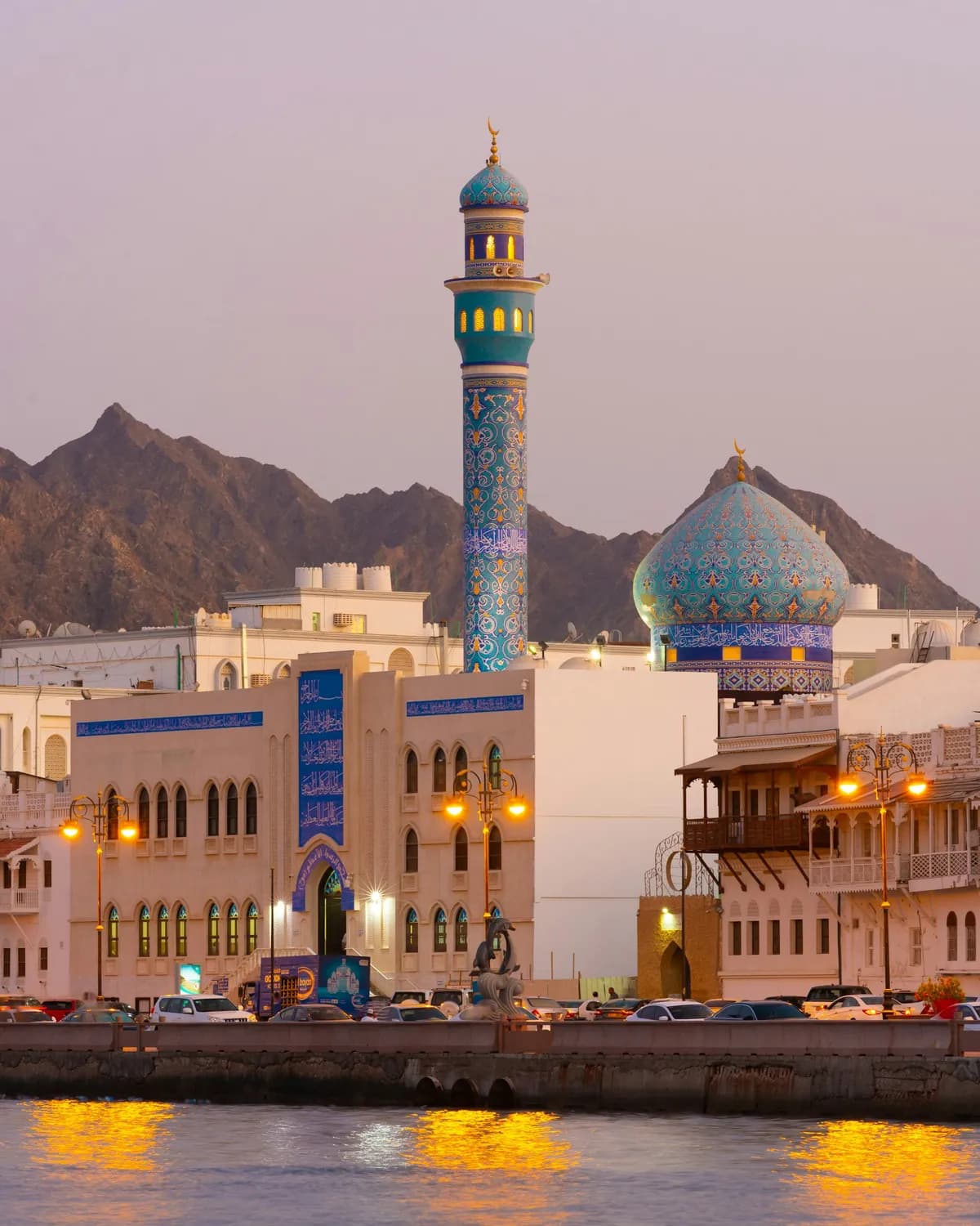 The blue-tiled minaret and dome of the Al Lawatiya Mosque on the Muttrah Corniche at dusk, Muscat