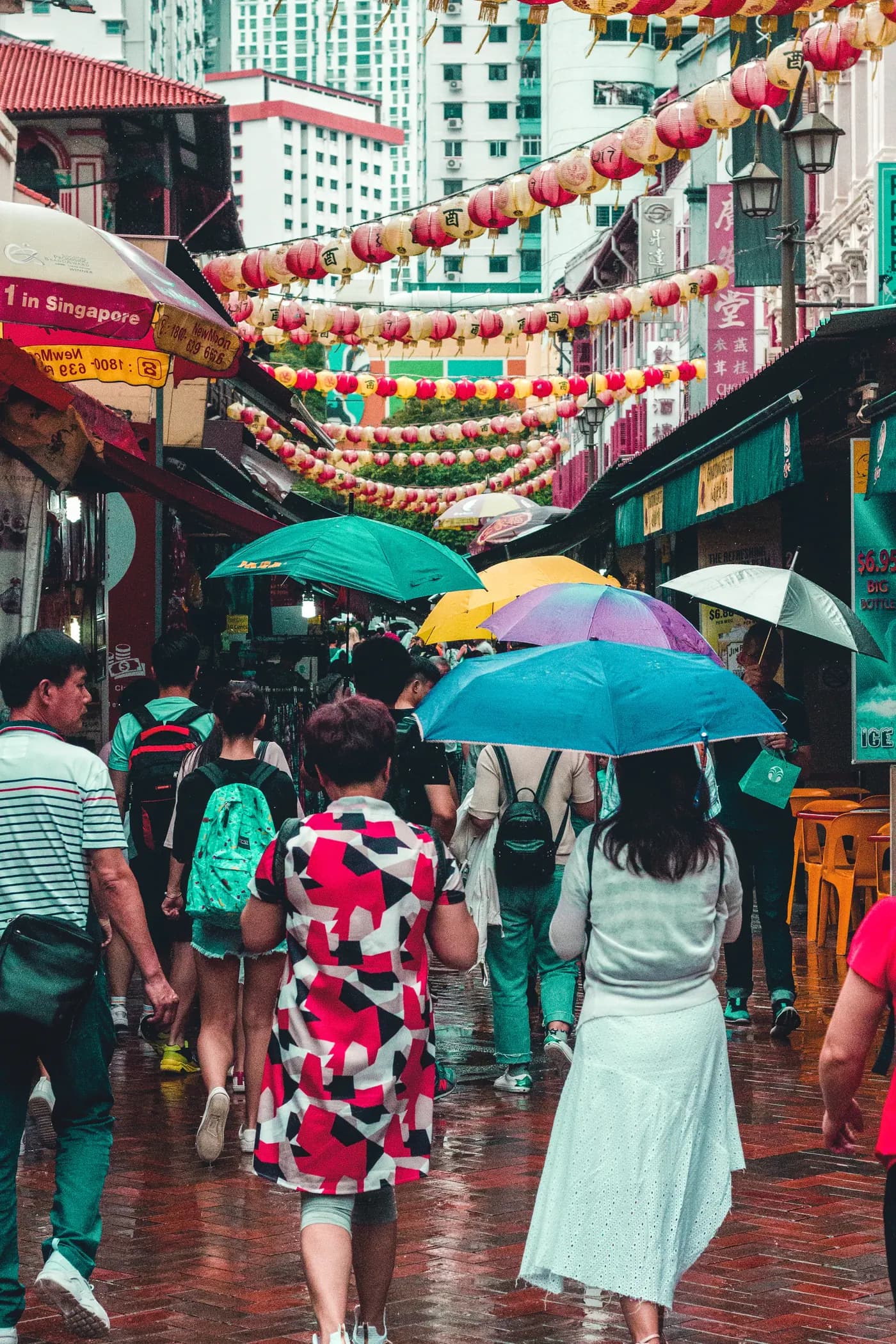 Shoppers under umbrellas on a lantern-hung street in Chinatown
