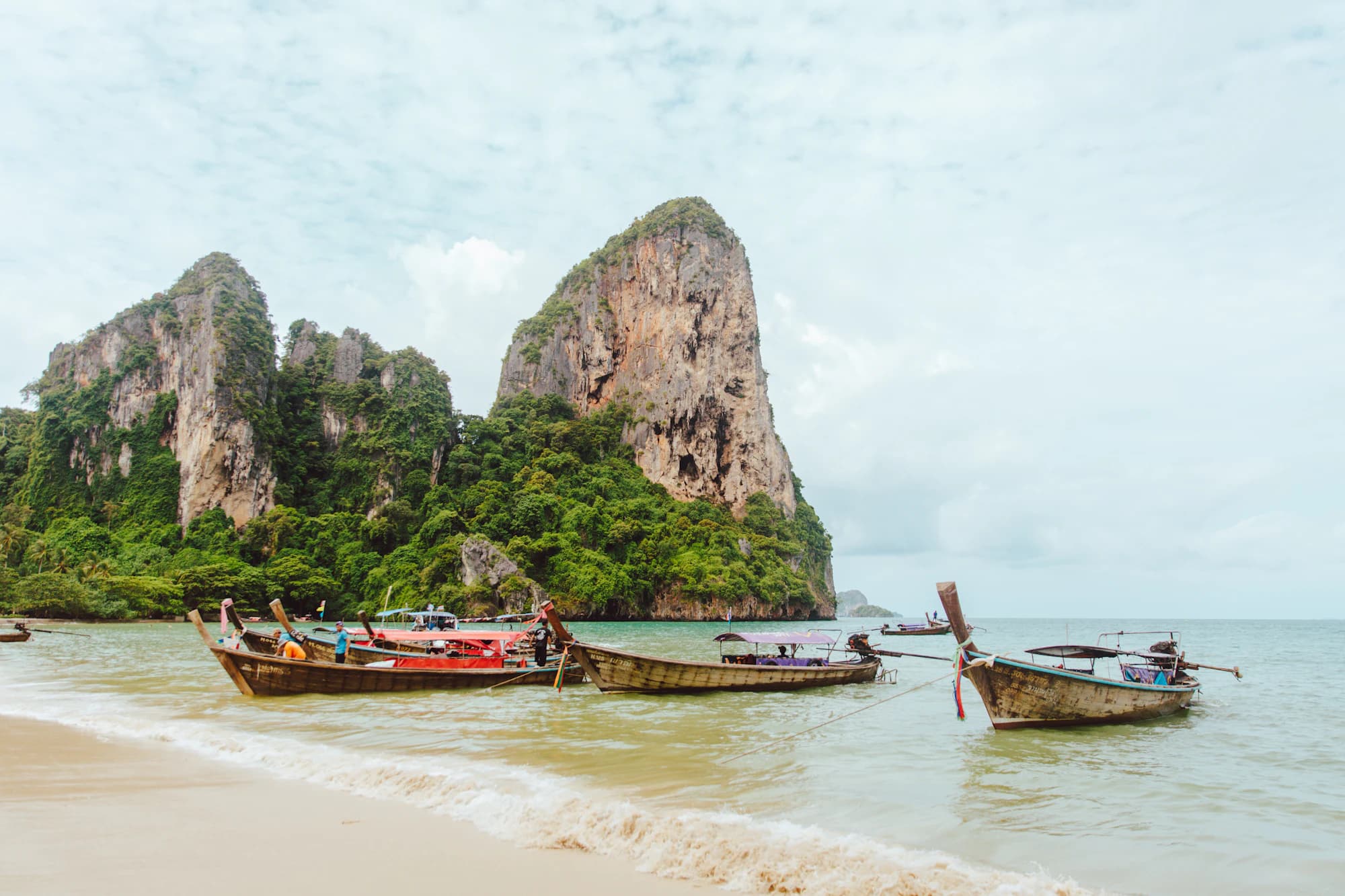 Longtail boats pulled up on Railay beach below its limestone cliffs, Krabi