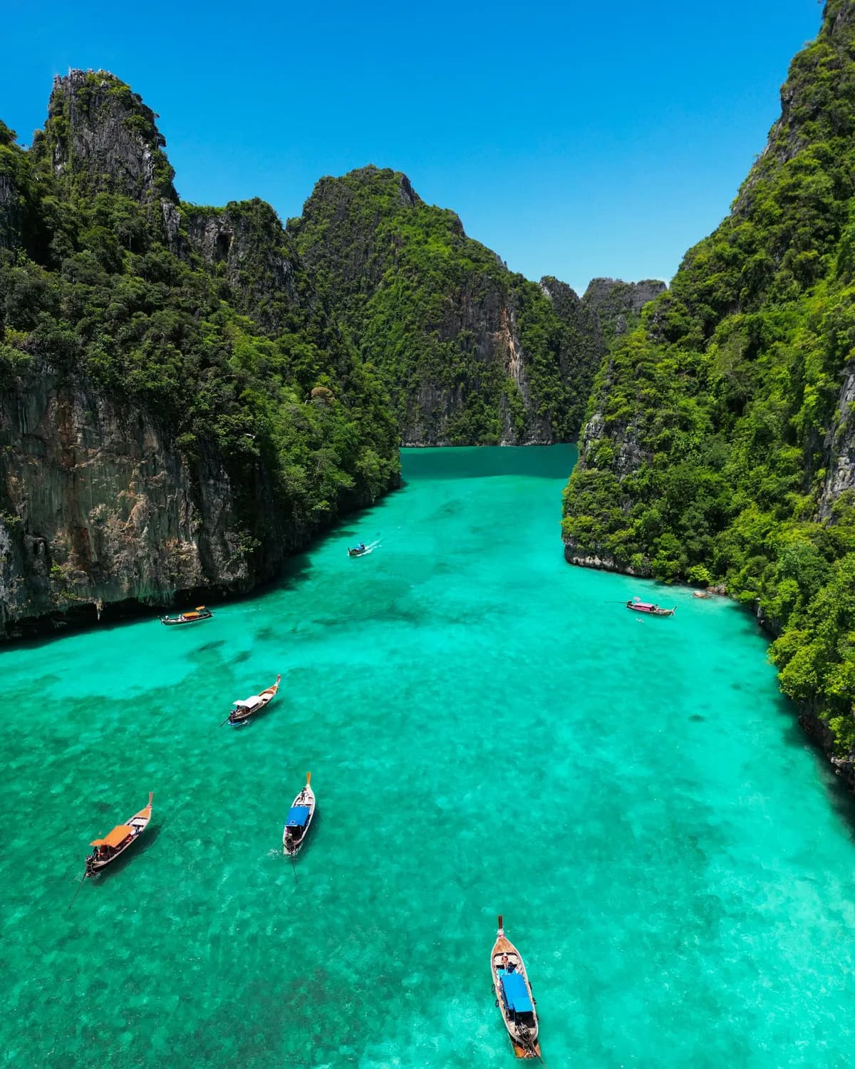 Longtail boats on the turquoise water of Pileh Lagoon between limestone cliffs, Phi Phi Islands