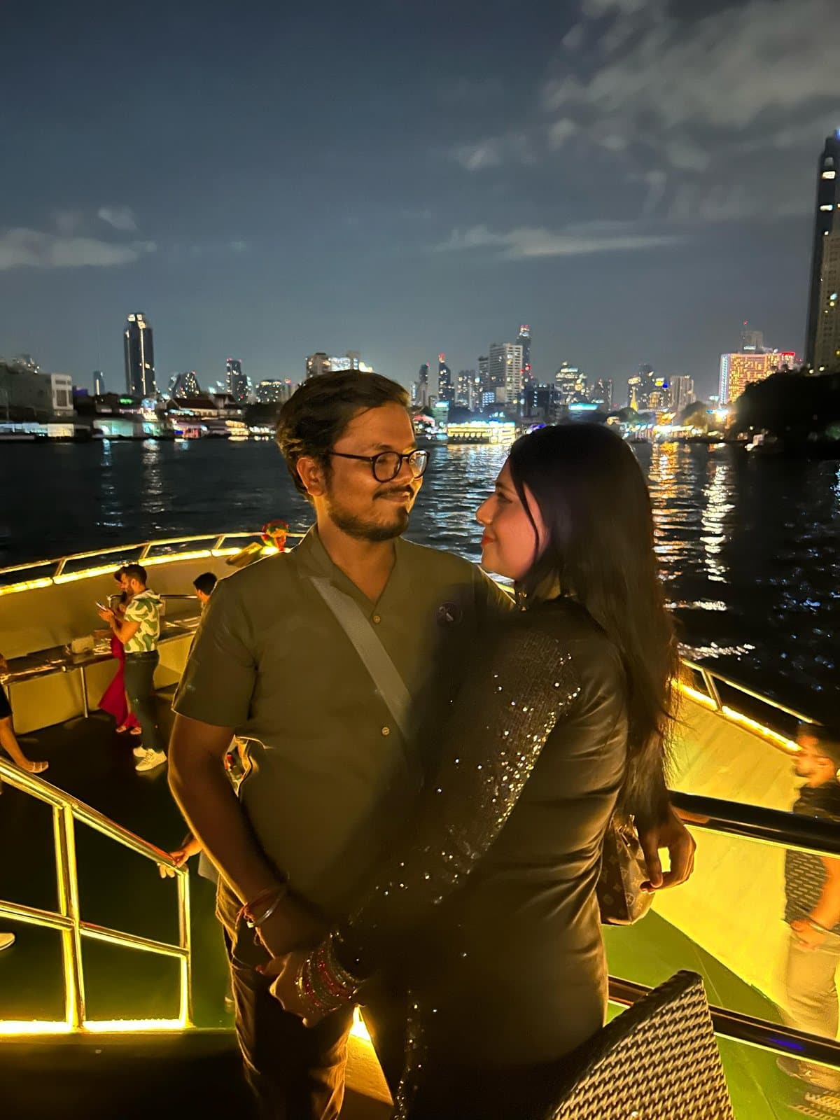 A couple on a night river cruise past the Bangkok skyline